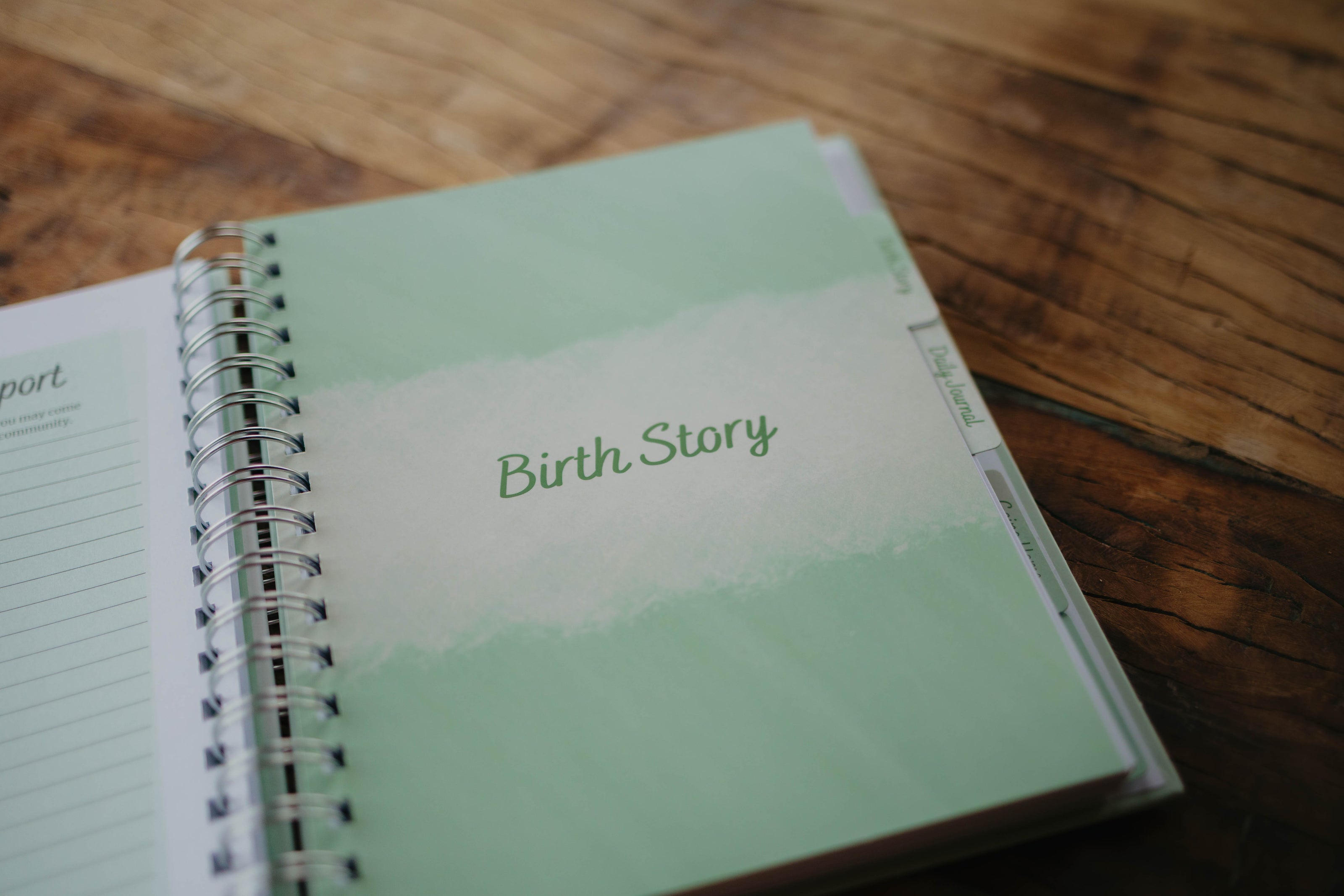 A close up of the Birth Story  section tab page in The NICU Notebook®, a light green, coil bound NICU Journal for families with a baby in the Neonatal Intesive Care Unit, on a wooden table top.