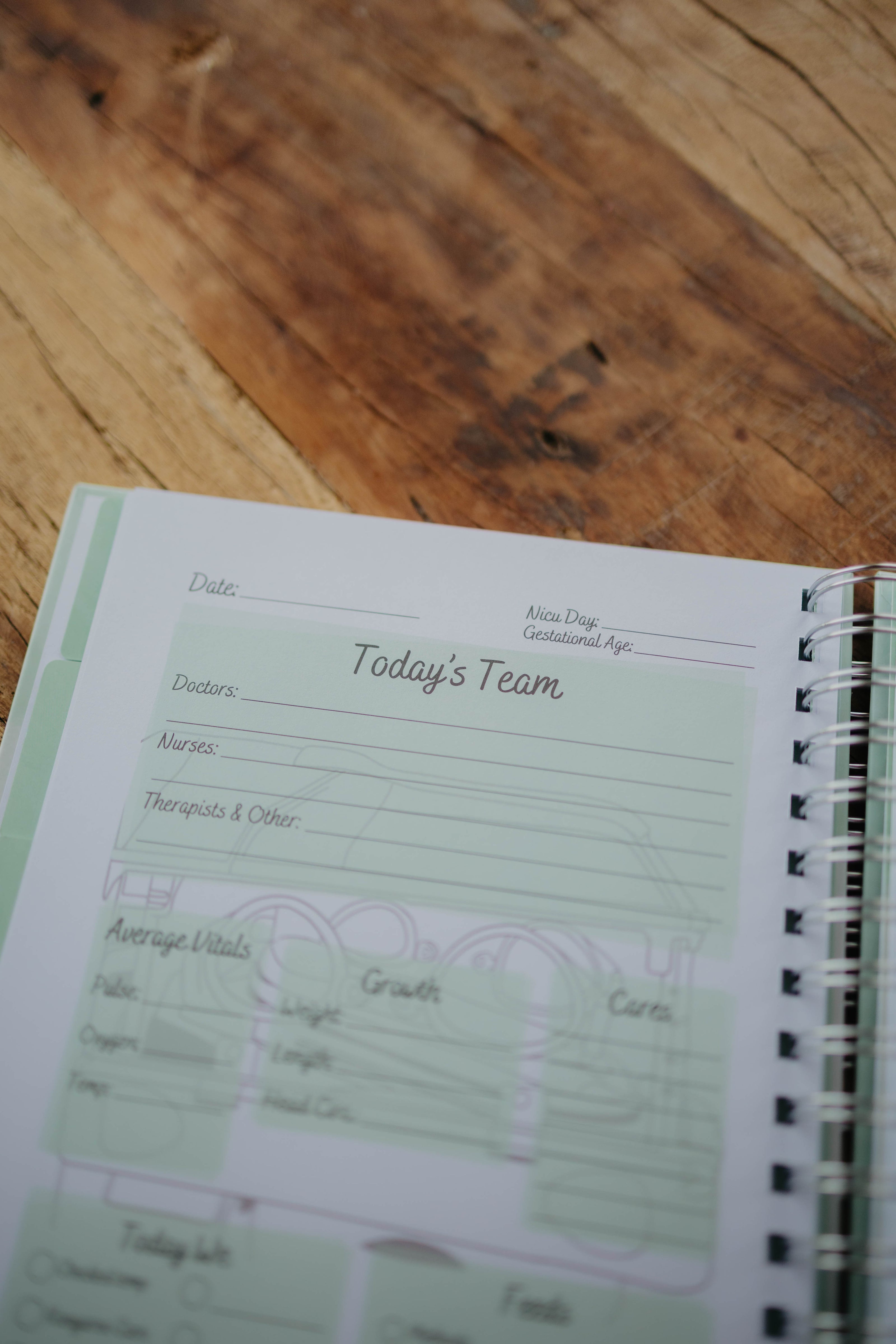 The NICU Notebook®, a light green, coil-bound NICU Journal, opened to a page from the Daily Journal section. The page features unfilled boxes that hold information such as 