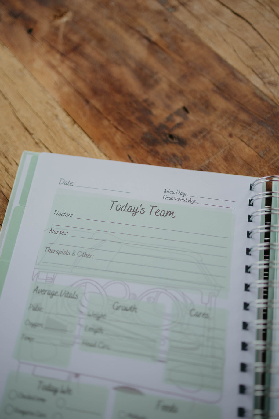 The NICU Notebook®, a light green, coil-bound NICU Journal, opened to a page from the Daily Journal section. The page features unfilled boxes that hold information such as 