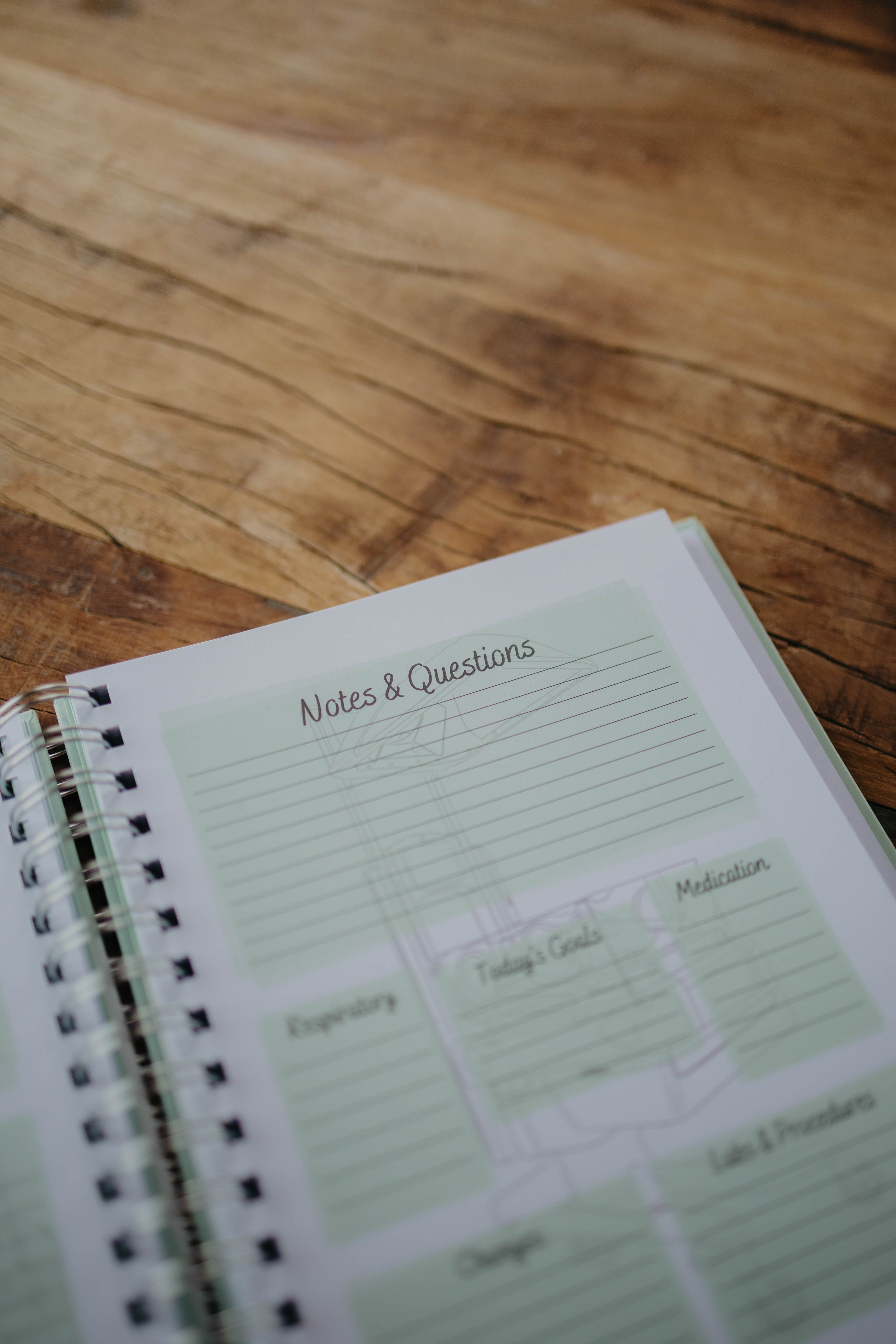The NICU Notebook®, a light green, coil-bound NICU Journal, opened to the second daily page from the Daily Journal section. The page features unfilled boxes that hold information such as 
