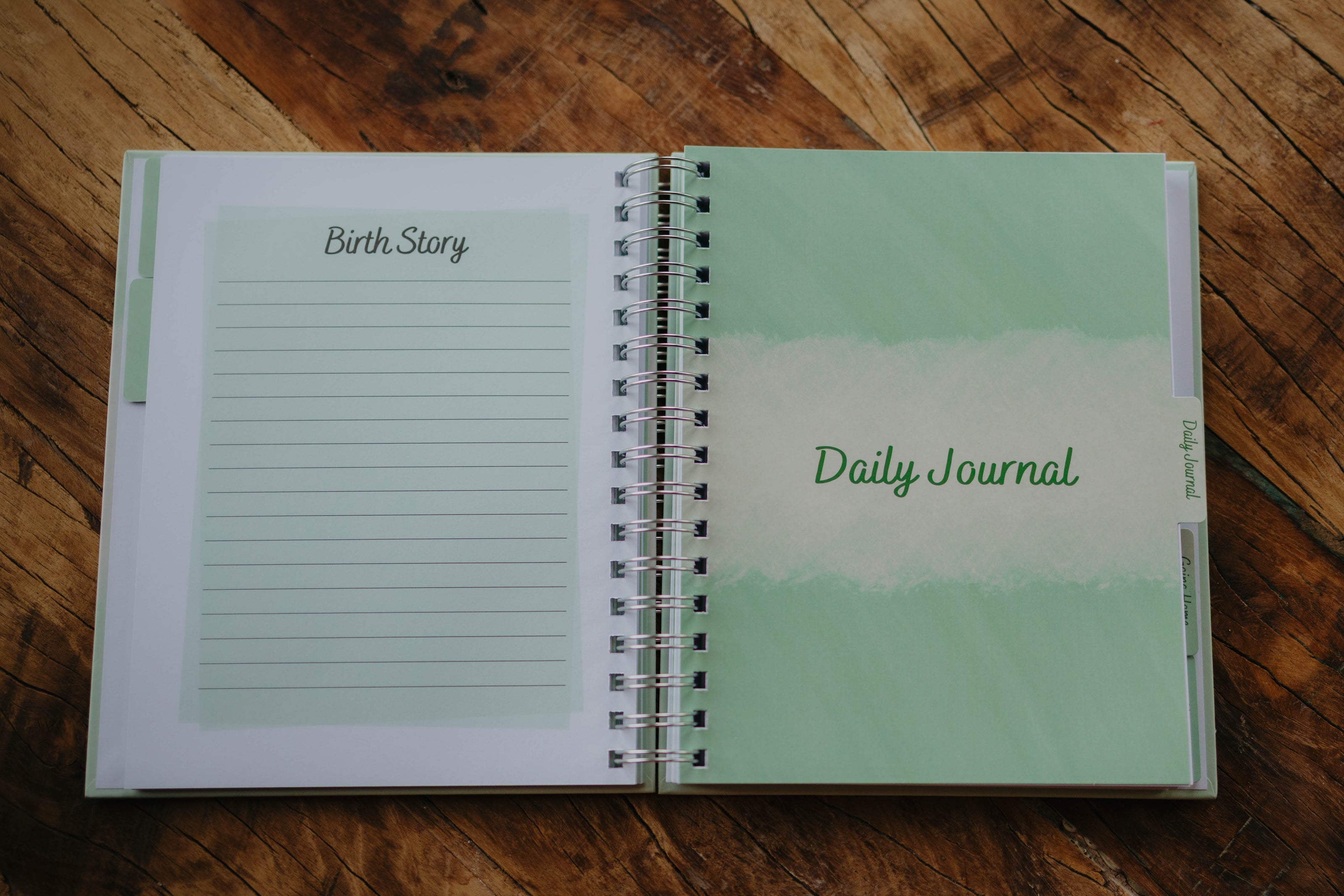 A close up of the last lined page in the Birth Story section and the Daily Journal tab page in The NICU Notebook®, a light green, coil bound NICU Journal for families with a baby in the Neonatal Intesive Care Unit, on a wooden table top.