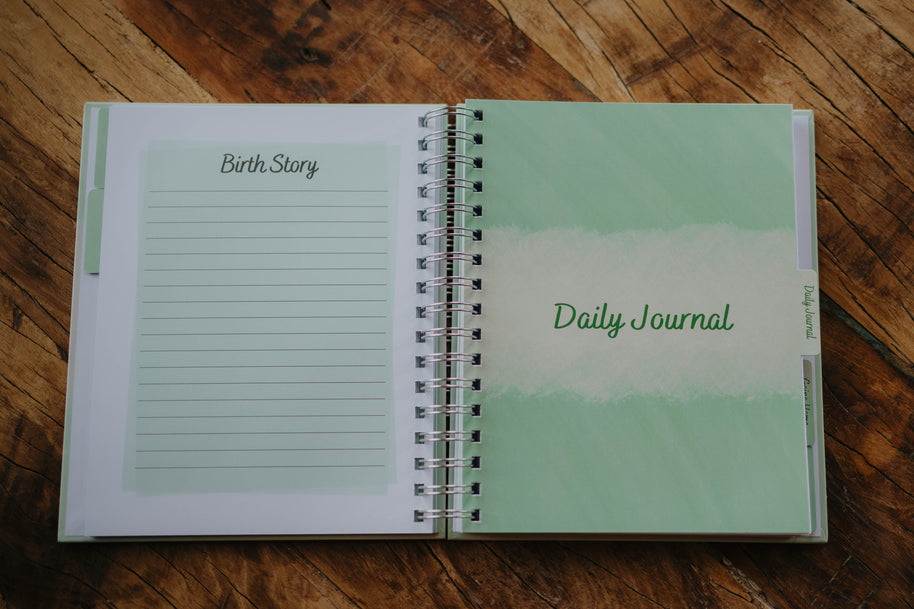 A close up of the last lined page in the Birth Story section and the Daily Journal tab page in The NICU Notebook®, a light green, coil bound NICU Journal for families with a baby in the Neonatal Intesive Care Unit, on a wooden table top.